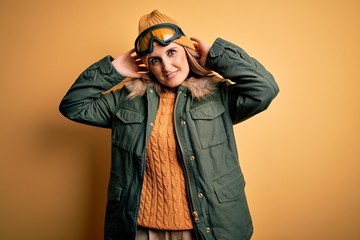 Middle age beautiful blonde skier woman wearing snow sportwear and ski goggles relaxing and stretching, arms and hands behind head and neck smiling happy