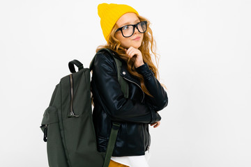 European attractive girl dressed in a yellow hat, glasses and a leather jacket with a backpack on her back on a white background with copyspace