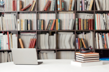 A stack of books with headphones on the background of a rack of books in the reading room of the library. Student poster