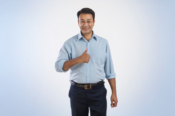 Portrait of a smiling businessman in eyeglasses showing a thumbs up sign
