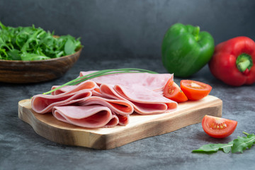 Breakfast with ham slices isolated on cutting board with fresh vegetables over dark background.