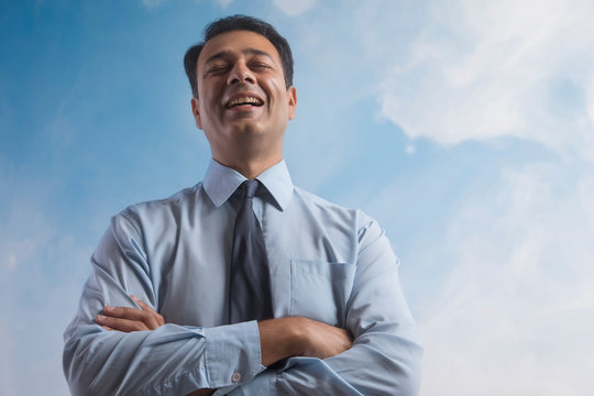 Smiling businessman with eyes closed standing with his arms crossed with sky in the background
