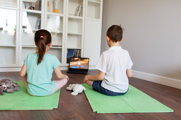 Kids doing yoga at home online laptop workout in flat. Baby yoga,fitness training. Quarantine, coronavirus, covid-19. No equipment.