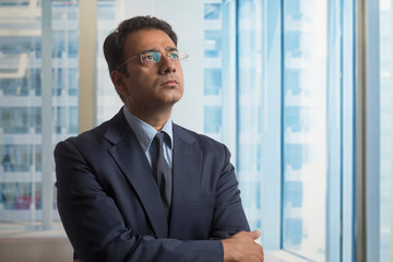 Businessman in formal clothes and eyeglasses thinking deeply looking away with arms crossed
