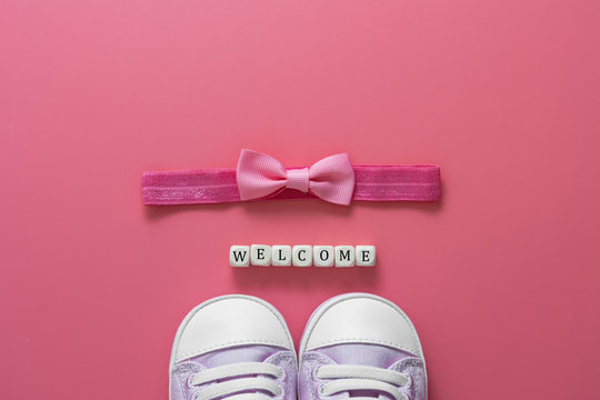 Baby girl pink background with newborn shoes, bow and Welcome words. Baby flat lay.