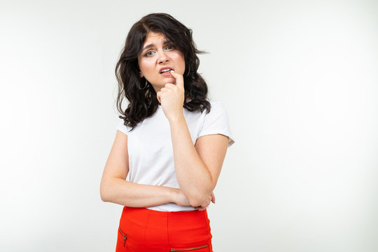 brunette girl in a white t-shirt worries and bites her nails from stress on a white background