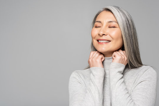 Happy Asian Woman In Turtleneck With Grey Hair And Closed Eyes Isolated On Grey