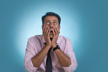 Businessman holding his face with both hands looking up with an expression of shock
