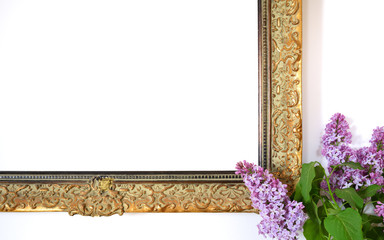 An antique frame without a picture in front of a white wall with lilac draped on the side