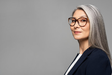 elegant asian businesswoman with grey hair in eyeglasses isolated on grey - obrazy, fototapety, plakaty
