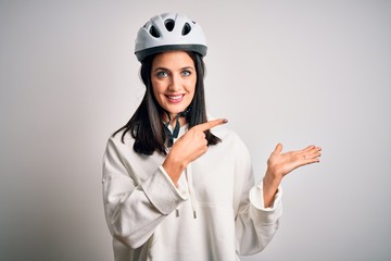 Young cyclist woman with blue eyes wearing bike helmet over isolated white background amazed and smiling to the camera while presenting with hand and pointing with finger.