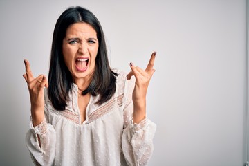 Young brunette woman with blue eyes wearing casual t-shirt over isolated white background shouting with crazy expression doing rock symbol with hands up. Music star. Heavy concept.