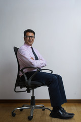 Smiling businessman in eyeglasses and formal wear sitting on revolving chair with arms crossed
