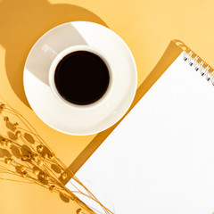 Top view sunny orange desktop with a blank notebook and a cup of coffee. Flat lay, minimal....