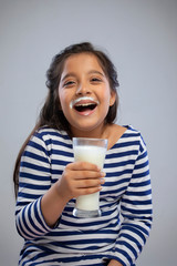 Portrait of a smiling girl with milk moustache holding a glass of milk
