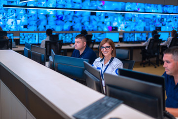 Happy security data center operator colleagues (coworkers) smiling and monitoring the CCTV footage while typing on a keyboard.
