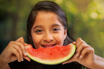 Close up of a girl eating a slice of watermelon holding with both hands
