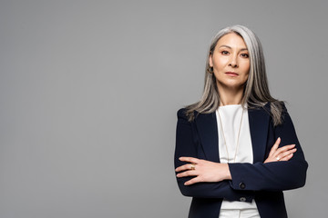 confident asian businesswoman with grey hair and crossed arms isolated on grey - Powered by Adobe