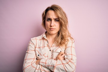 Young beautiful blonde woman wearing casual shirt standing over isolated pink background skeptic...