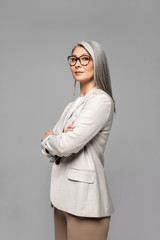 beautiful asian businesswoman in eyeglasses with crossed arms isolated on grey