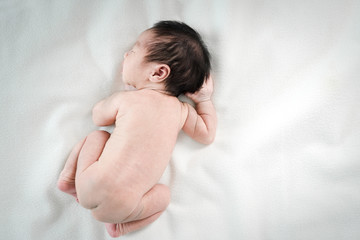 Asian newborn baby lying asleep on white blanket.