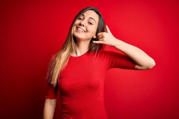 Young beautiful blonde woman with blue eyes wearing casual t-shirt over red background smiling doing phone gesture with hand and fingers like talking on the telephone. Communicating concepts.