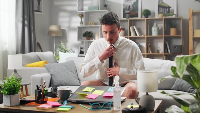 A young man works at home with a laptop without pants, during quarantine. Living room as an office.