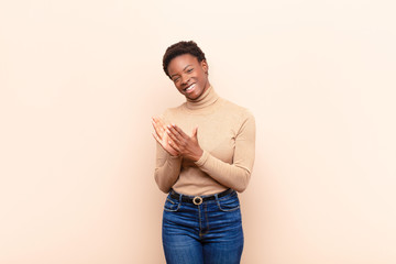 young pretty black womanfeeling happy and successful, smiling and clapping hands, saying...