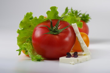 Pink tomato and sliced feta cheese lies among yellow cherry tomatoes, lettuce leaves and microgreen. Close-up. Gray background. Selective focus.