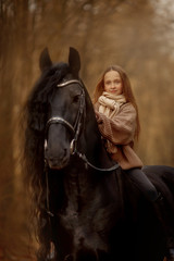 Little girl with Friesian stallion with long hair outdoor portrait in an autumn forest