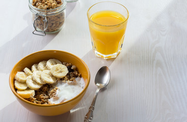 Healthy breakfast - granola with banana and yogurt, orange juice on a white wooden background.