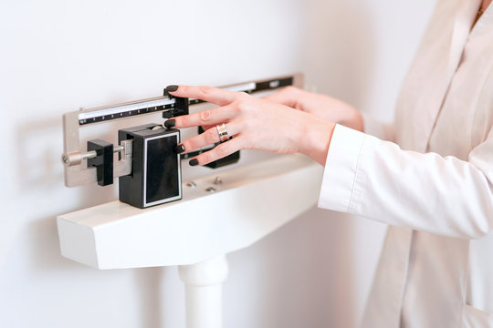 Closeup view of woman's hand adjusting professional balance weight scale. View is closeup, with a neutral background.