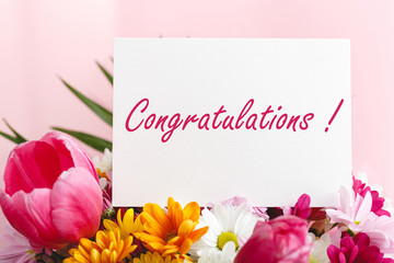 Congratulations text on gift card in flowers bouquet on pink background. White blank card with space for text, frame mockup. Spring festive flower concept, gift card
