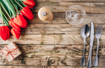 Spring rustic table setting with red tulip, glass and vintage cutlery on the wooden background.