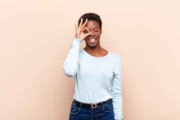 young pretty black womansmiling happily with funny face, joking and looking through peephole,...