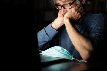 middle-aged man looking on computer at the news about global pandemic from corona virus and he worries, emotional distress, insomnia, concern for business and health in time of covid19