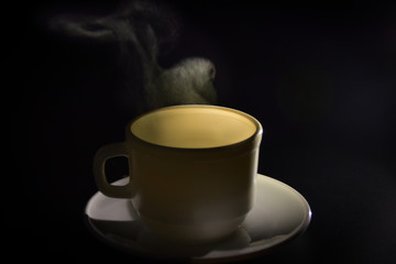 A cup of hot steaming tea on black background.