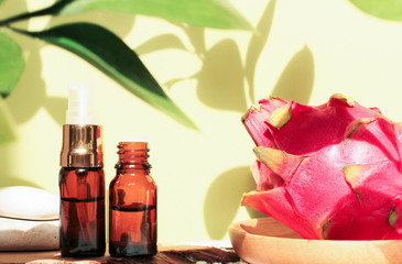 Tropical spa set with plant shadows green background, pitaya dragon fruit skin care extract, dark glass dropper bottles of essential oil, facial cosmetic product
