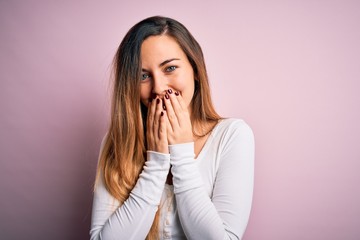 Young beautiful blonde woman with blue eyes wearing white t-shirt over pink background laughing and...