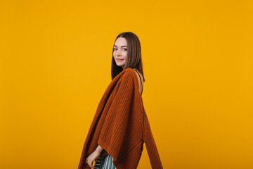 Naklejka premium Shy brunette girl posing in brown knitted sweater. Indoor portrait of interested european woman isolated on yellow background.