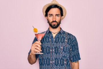 Young handsome hispanic bohemian hipster man with bear drinking a summer cocktail with a confident expression on smart face thinking serious