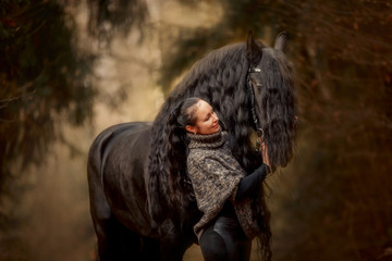 Woman with Black Beautiful  Friesian stallion with long hair outdoor portrait in an autumn forest