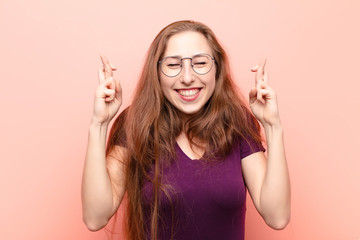 yound blonde woman smiling and anxiously crossing both fingers, feeling worried and wishing or...