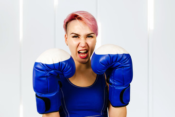 Beautiful young woman in blue boxing gloves is boxing on a light background.