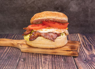 Tasty fresh burger with bacon, eggs, tomatoes and lettuce, on a wooden board