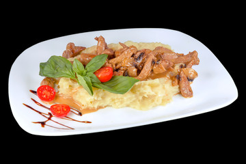 Tasty meat in small pieces on mashed potatoes with cherry tomatoes, on a white plate, isolated on black background