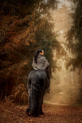 Woman with Black Beautiful  Friesian stallion with long hair outdoor portrait in an autumn forest