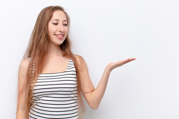 yound blonde woman feeling happy and smiling casually, looking to an object or concept held on the...