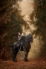 Mother and daughter  with Black Beautiful  Friesian stallion with long hair outdoor portrait in an autumn forest