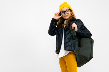 European attractive girl dressed in a yellow hat, glasses and a leather jacket with a backpack on her back on a white background with copyspace